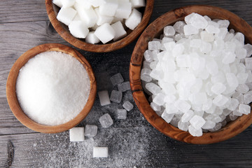 Bowl with white sand, crystal and lump sugar on wooden background.