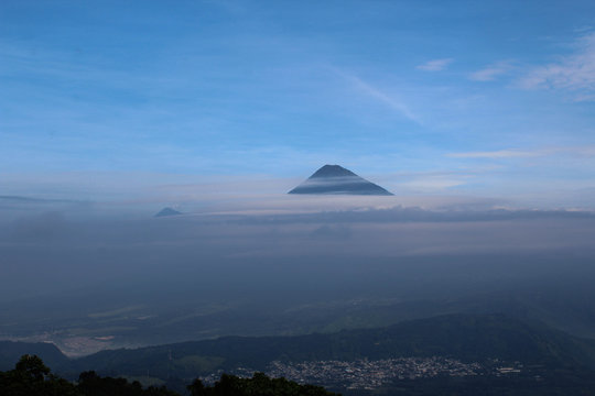 Sullo sfondo la cima del vulcano de Fuego che spunta dalle nuvole e svetta nel cielo azzurro, Guatemala 