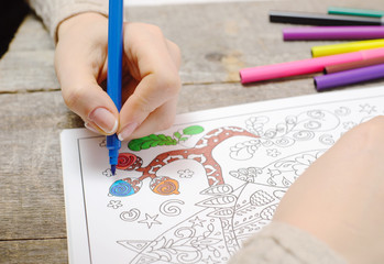 An image of a new trendy thing called adults coloring book. In this image a person is coloring an illustrative and detailed pattern for stress relieve for adults.
