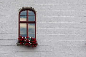A beautiful arched wooden window decorated with red and white flowers on a neutral grey facade