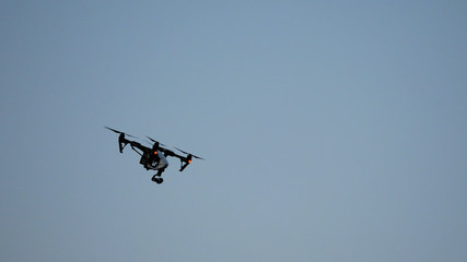 Fototapeta premium Black drone quadcopter with camera flying over blue sky. Black drone in the sky. Flying quadrocopter drone in the sky with mounted digital camera for video and photo productions