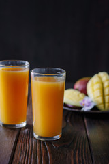 Fresh tropical mango juice on table with mango fruits on background.