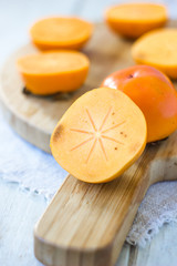 Half of persimmon fruit on wooden board.
