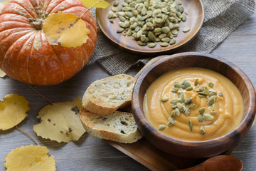 Pumpkin soup in a wooden bowl, with autumn leaves and pumpkin