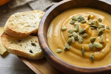 Pumpkin soup in a wooden bowl, with autumn leaves and pumpkin