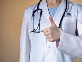 Female doctor showing thumb up. Female doctor with a stethoscope gesticulating on a beige background.