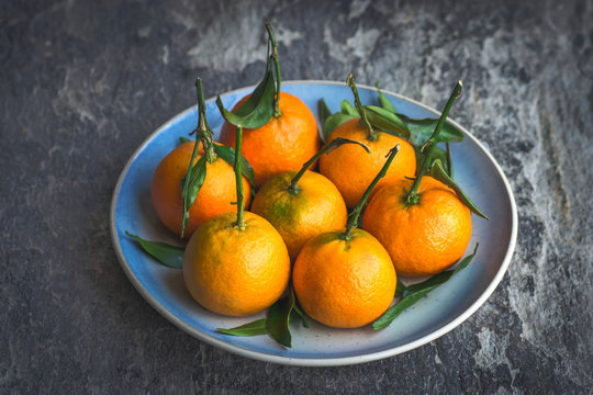 Ripe mandarins with leaves on a blue plate and a textured background