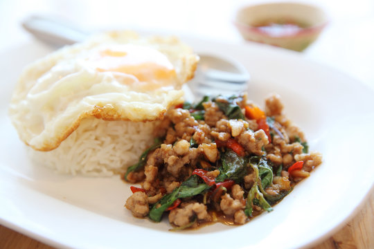 stir fried pork and basil with rice and egg on wood background thai food