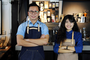 Portrait of smiling asian barista team with arms crossed at counter in coffee shop. Cafe restaurant...