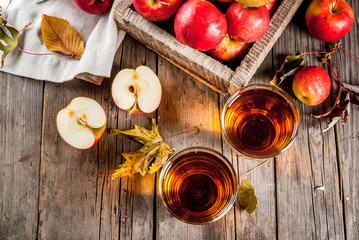 Fresh organic farm apple juice in glasses with raw whole and sliced red apples, on old rustic wooden table, copy space top view