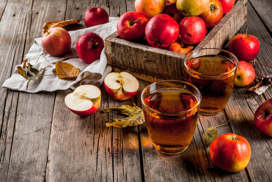 Fresh organic farm apple juice in glasses with raw whole and sliced red apples, on old rustic wooden table, copy space