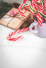Christmas time concept, Christmas tree branches, pine cones, gifts and traditional New Year sweets candy cane, on a white marble table with snow. Copy space