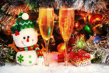 merry snowman and wineglasses with sparkling wine on the background of a Christmas tree. balls, garlands, tinsel. Christmas and New Year with champagne