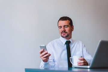 Mature businessman in suit using cell phone at desk in small office.