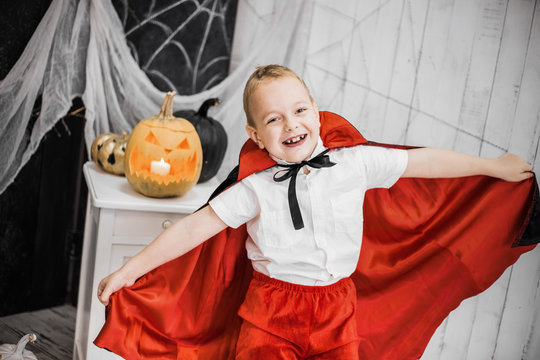Portrait of funny cute little boy playing cheerfully in costume of vampire in beautiful spooky Halloween decor in black and white colors. Horizontal color photo.