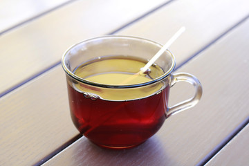 transparent glass cup of black tea staying on the wooden  table of outdoor  cafe.