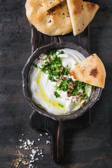 labneh middle eastern lebanese cream cheese dip with olive oil, salt, herbs served traditional pita bread in terracotta bowl over dark texture metal background. Top view with space