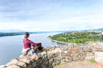 Young woman traveller sitting on top mountain contemplating spectacular view