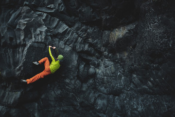 male rock climber. rock climber climbs on a black rocky wall on the ocean bank in Iceland,...