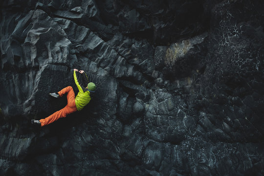 male rock climber. rock climber climbs on a black rocky wall on the ocean bank in Iceland, Kirkjufjara beach. man makes hard move without rope.
