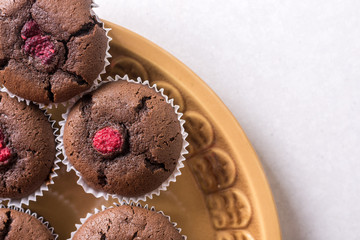 Flat lay above plate with chocolate cup cake muffins with raspberries with white copy space background