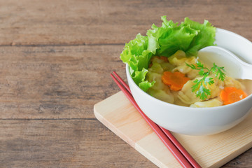 Homemade minced pork and shrimp wonton soup in white bowl on wood table with copy space. Delicious wonton in clear soup for breakfast or lunch or dinner .Wonton or dumpling is popular Chinese food.