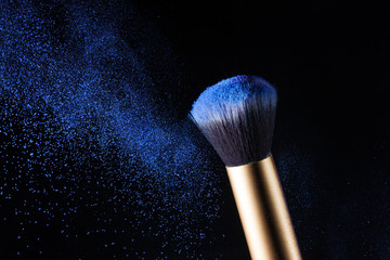 Cosmetics makeup brush and powder dust explosion. Isolation on a black background.