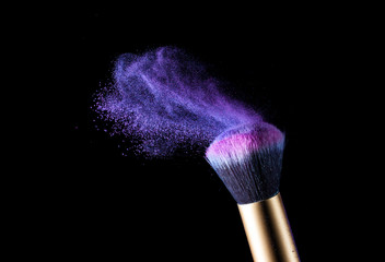 Make-up brush with pink powder explosion isolated on black background