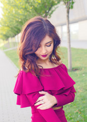 Woman cute posing. Beauty romantic girl outdoor. Pretty brunette curly young model dressed in pink dress posing outdoors in the park background.Portrait of young stylish beautiful girl. Model portrait