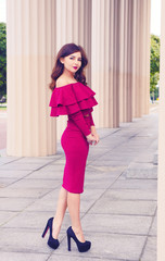 Fototapeta na wymiar Cute posing girl in fashion look with pink dress stands on the background of nature and architectural Greek columns. Young long hair caucasian female model in pink fashionable dress and pretty make up