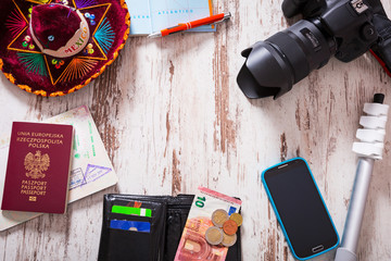 Travel background with a camera, touristic maps, passport, mobile phone, headphones, wallet with credit cards, euro money, tripod and sombrero on wooden desk.
