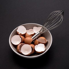 Fototapeta na wymiar eggshells and beater in a white bowl on a black table