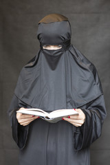 Woman in burqa reading book against black background