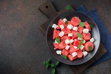 Salad with watermelon and feta cheese with mint on a black ceramic plate. Traditional Mediterranean Italian salad. Selective focus. Top view.