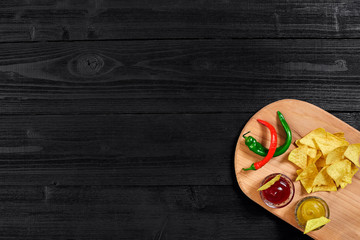 Tortilla chips with mustard and tomato sauce on black wooden table. Top view