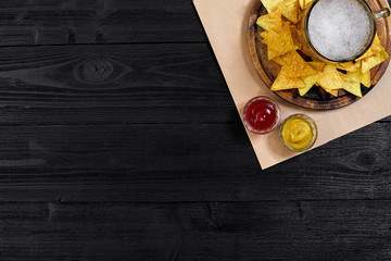 Glass of beer with nachos chips on a wooden background.