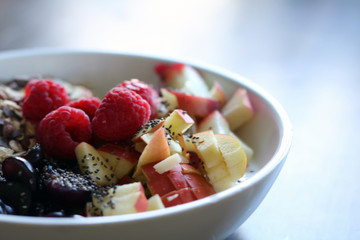 mixed fruit and cereal in a white bowl on brown wooden table