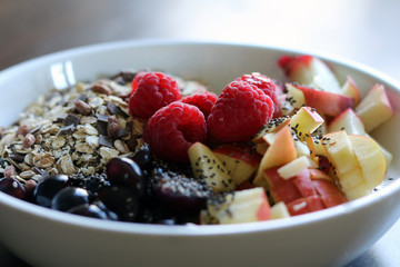 mixed fruit and cereal in a white bowl on brown wooden table