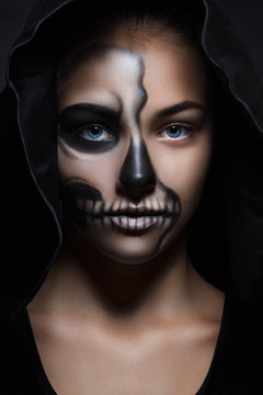 Halloween portrait of young beautiful girl in a black hood. skeleton makeup half face