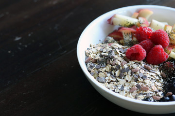 mixed fruit and cereal in a white bowl on brown wooden table