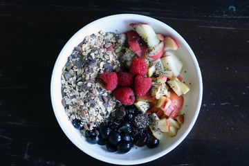 mixed fruit and cereal in a white bowl on brown wooden table
