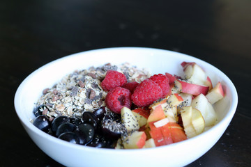mixed fruit and cereal in a white bowl on brown wooden table