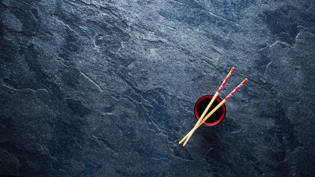 Chopsticks and bowl with soy sauce on textured background