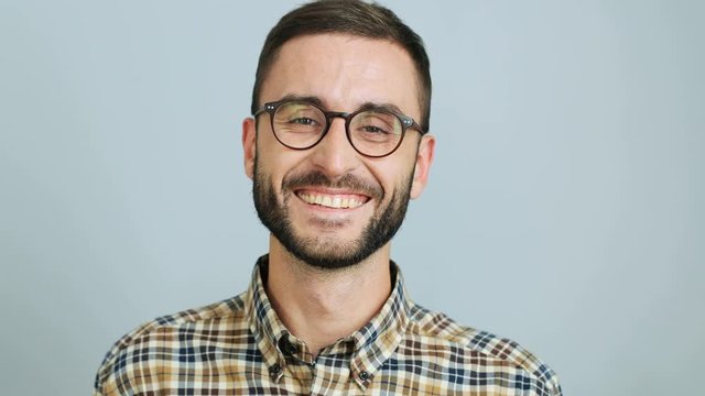 Close up shot of a young handsome man in a casual shirt smiling and showing cheerful emotions at the camera on the grey background. Outdoor shot.