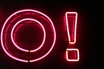 Red neon light letter and exclamation point (mark) on a black wall