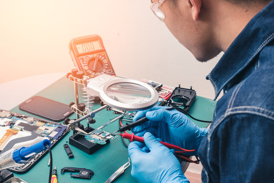 The abstract image of the asian technician repairing smartphone's motherboard by multimeter in the lab. the concept of computer hardware, mobile phone, electronic, repairing, upgrade and technology.