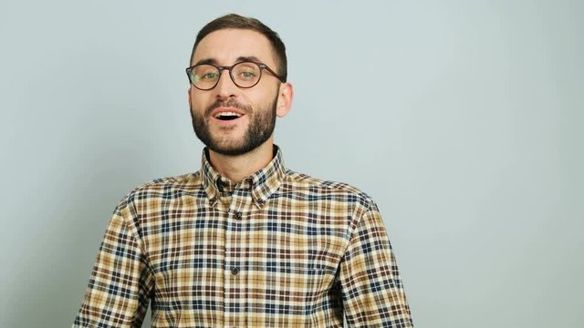 Close up shot of a young caucasian man in a casual shirt showing emotion of amasement and happiness on the grey background. Outdoor shot.