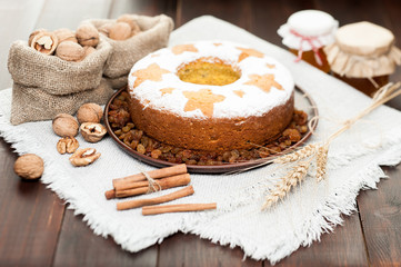 Fototapeta na wymiar homemade traditional fruit cake on clay plate decorated with wheat ears, nuts, cinnamon and honey jars at wooden table