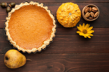 pumpkin homemade pie at wooden background decorated with nuts, pear and flower top view