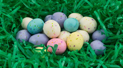 A group of speckled Easter egg malt ball candies nestled in a green plastic grass.